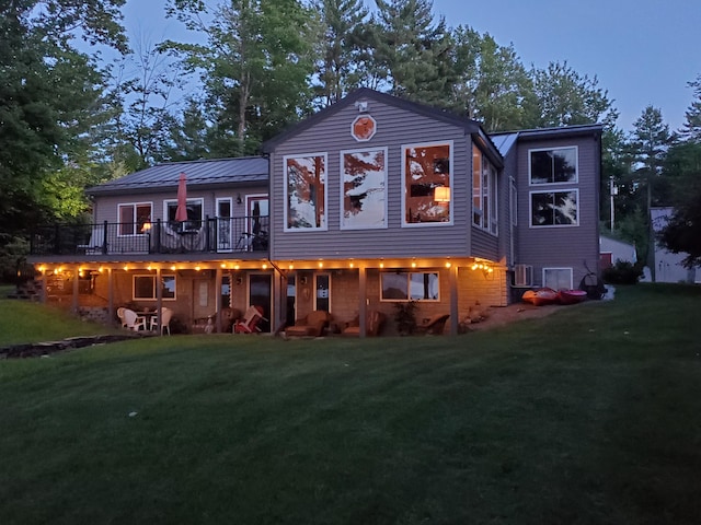 back house at dusk featuring a deck and a lawn