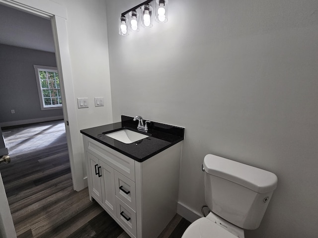 half bath with wood finished floors, toilet, vanity, and baseboards