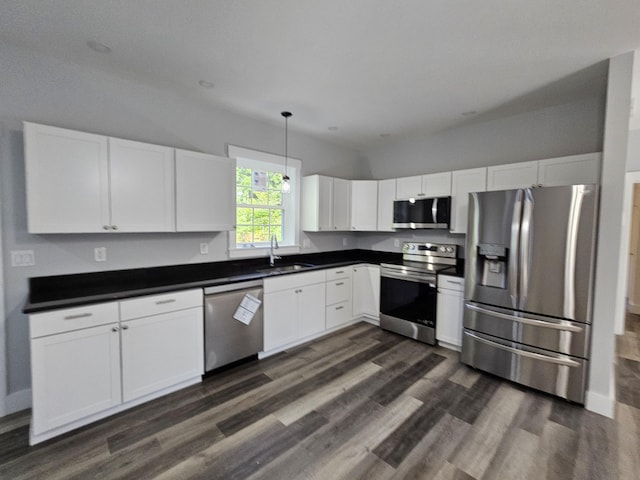 kitchen with appliances with stainless steel finishes, a sink, dark wood-style floors, dark countertops, and white cabinets