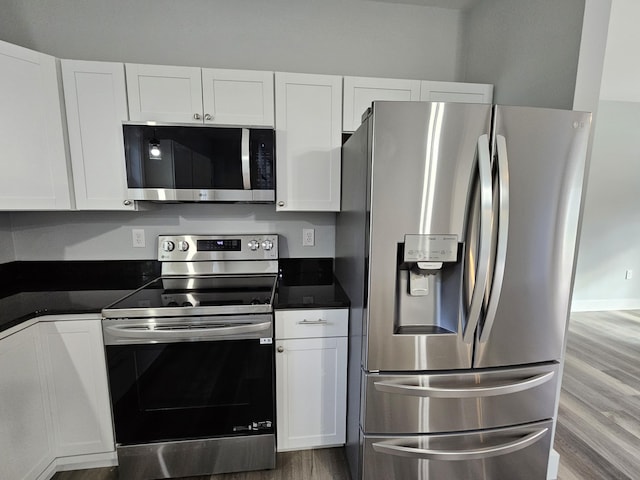 kitchen featuring stainless steel appliances, wood finished floors, dark countertops, and white cabinetry