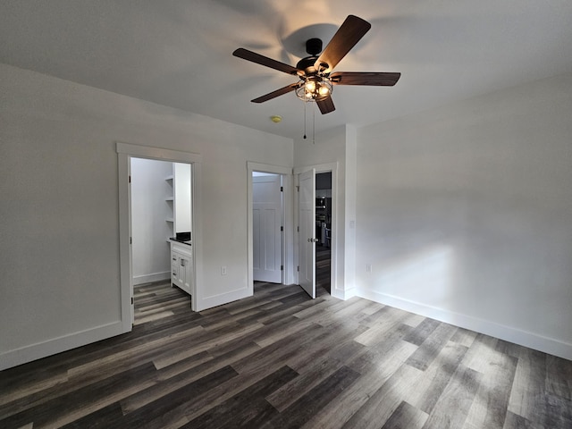 unfurnished bedroom with a spacious closet, dark wood-style flooring, baseboards, and a ceiling fan
