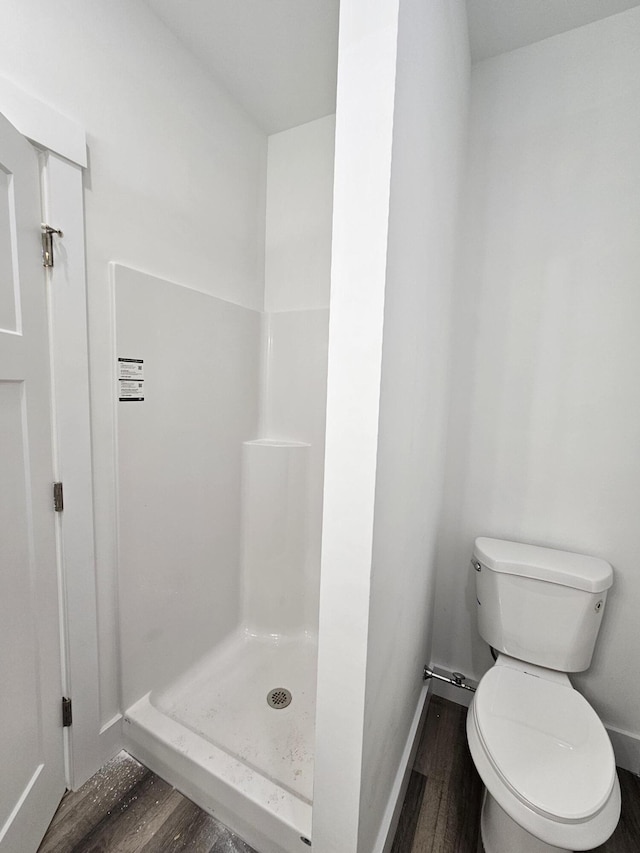 bathroom with wood finished floors, a shower stall, toilet, and baseboards