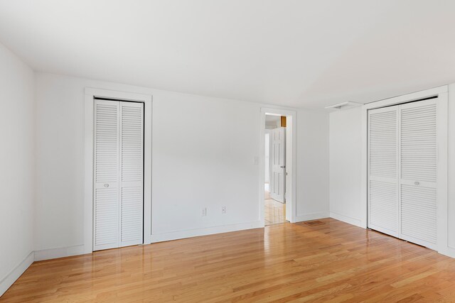 unfurnished bedroom with light hardwood / wood-style floors and two closets