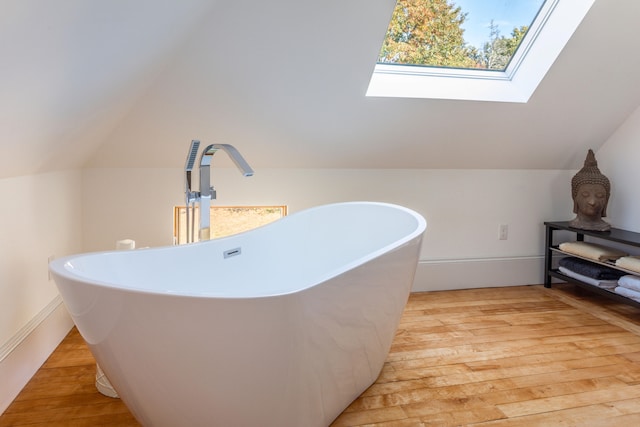 bathroom with vaulted ceiling with skylight, hardwood / wood-style floors, a tub to relax in, and sink