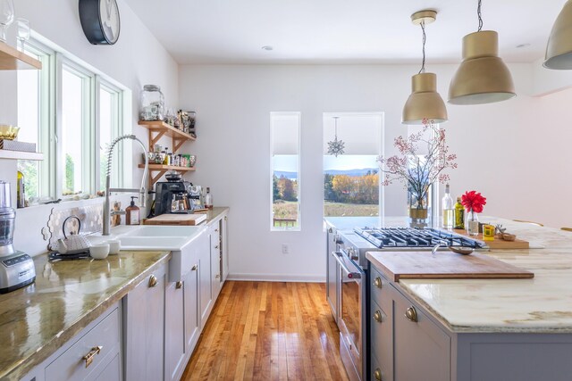 kitchen with high end range, gray cabinets, light hardwood / wood-style flooring, light stone counters, and hanging light fixtures