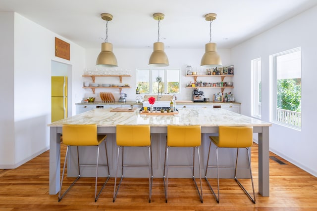 kitchen featuring light stone counters, white fridge, a kitchen bar, and light hardwood / wood-style flooring