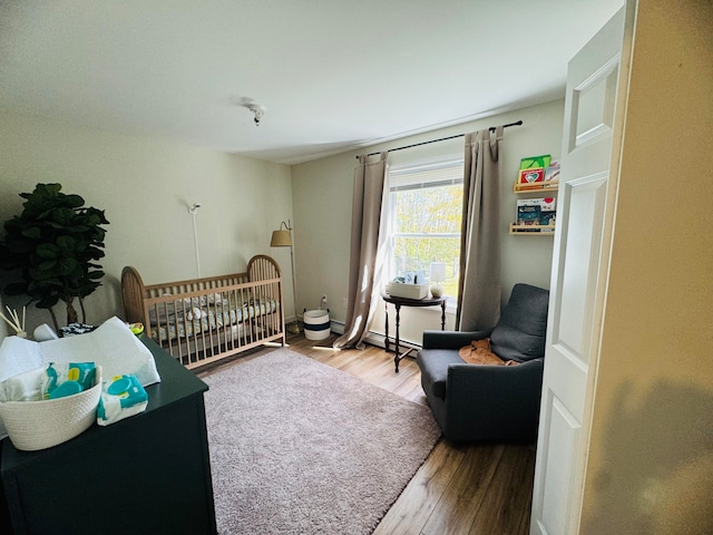 bedroom featuring baseboard heating, a nursery area, and wood finished floors