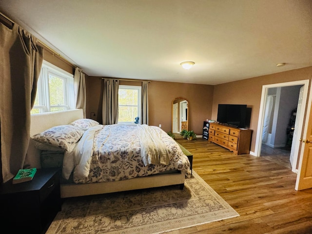 bedroom featuring baseboards, arched walkways, and wood finished floors