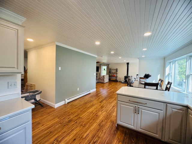 kitchen with gray cabinetry, a baseboard radiator, light countertops, a wood stove, and dark wood-style flooring