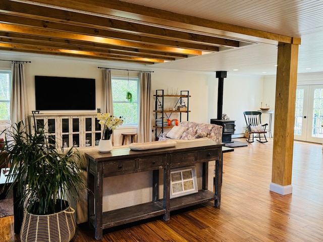 living area featuring beamed ceiling, wood finished floors, french doors, baseboards, and a wood stove