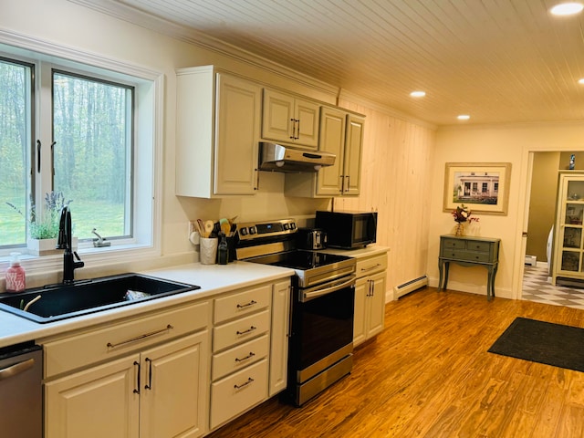 kitchen with crown molding, a baseboard heating unit, under cabinet range hood, appliances with stainless steel finishes, and a sink