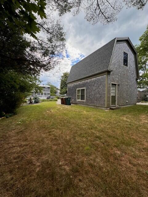 view of side of home featuring a shingled roof, a gambrel roof, and a lawn