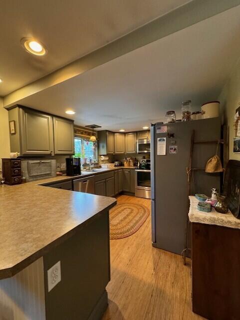 kitchen with a sink, light wood-type flooring, appliances with stainless steel finishes, a peninsula, and gray cabinetry