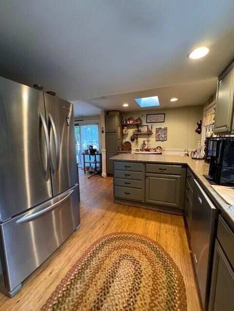 kitchen with a peninsula, light wood-style floors, gray cabinetry, stainless steel appliances, and a skylight