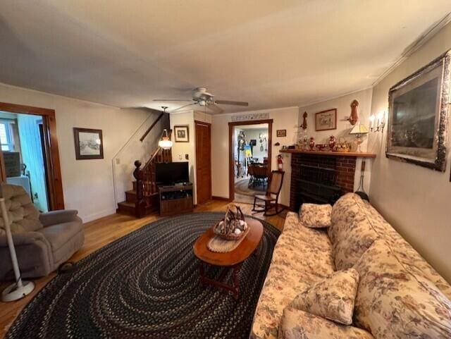 living room with stairs, a fireplace, a ceiling fan, and wood finished floors