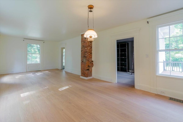 unfurnished room with light wood-type flooring, decorative columns, and plenty of natural light