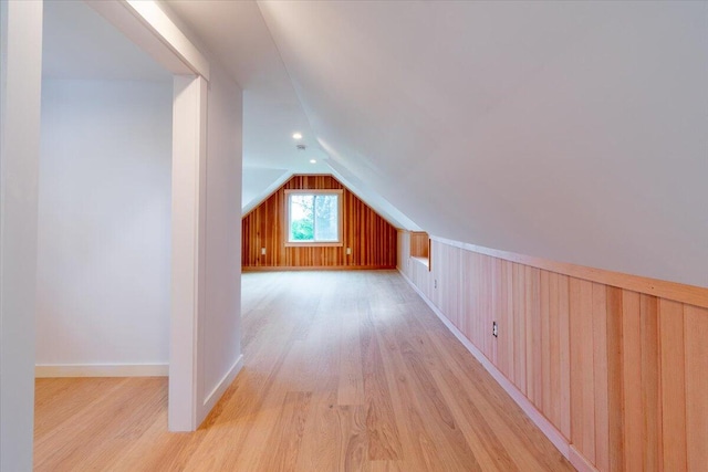 additional living space featuring wooden walls, light wood-type flooring, and vaulted ceiling