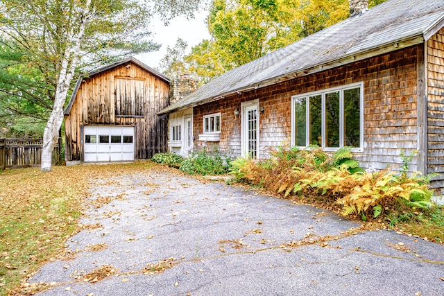 2457 Main St, Hanover, ME 04237 - view of home's exterior with driveway, a detached garage, an outbuilding, a chimney, and a shingled roof