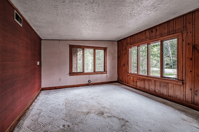 carpeted empty room featuring a textured ceiling, lofted ceiling, and wood walls