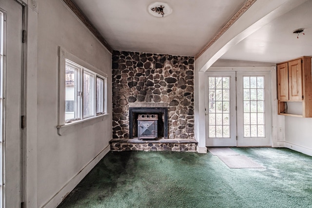 unfurnished living room featuring french doors, a stone fireplace, carpet, crown molding, and vaulted ceiling