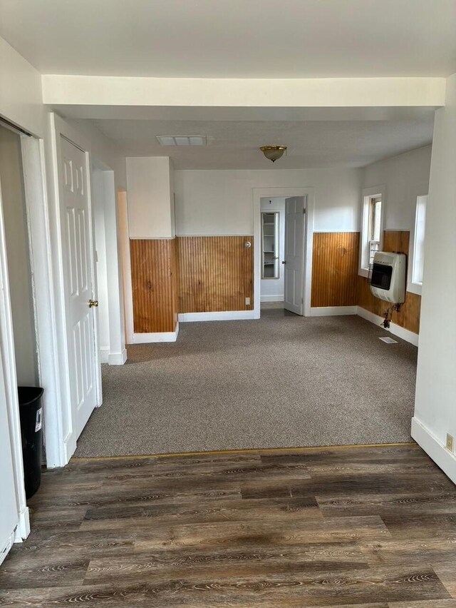 unfurnished room featuring heating unit, dark wood-type flooring, and wood walls