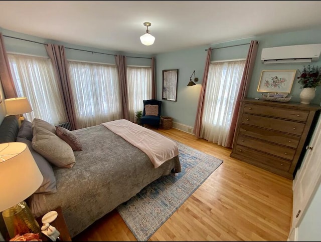 bedroom with light hardwood / wood-style flooring, multiple windows, and a wall unit AC