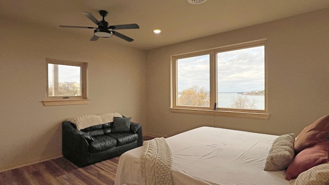 bedroom featuring ceiling fan, wood-type flooring, a water view, and multiple windows