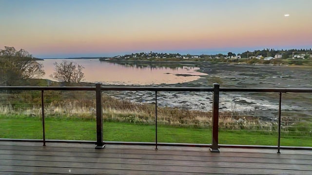 deck at dusk with a water view and a yard