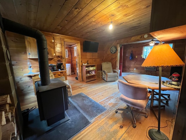 living room featuring light wood-type flooring, wooden walls, a wood stove, and wooden ceiling