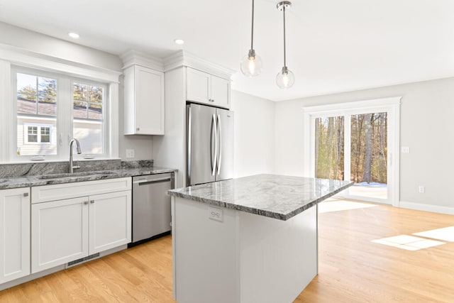 kitchen featuring white cabinets, light stone countertops, appliances with stainless steel finishes, a center island, and light wood-type flooring