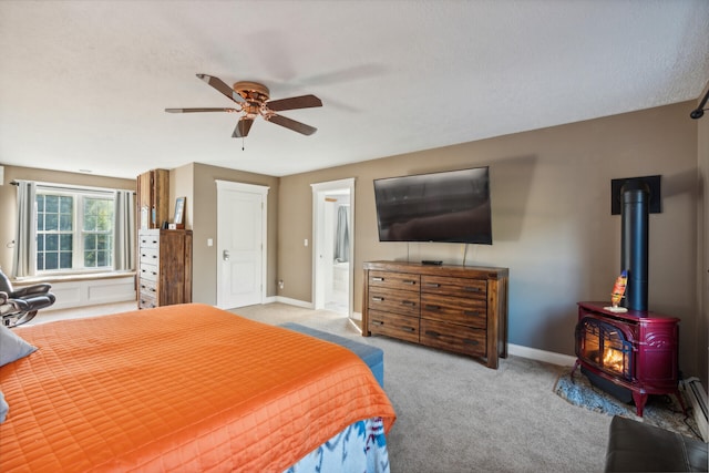 carpeted bedroom featuring a wood stove, ceiling fan, connected bathroom, and a textured ceiling