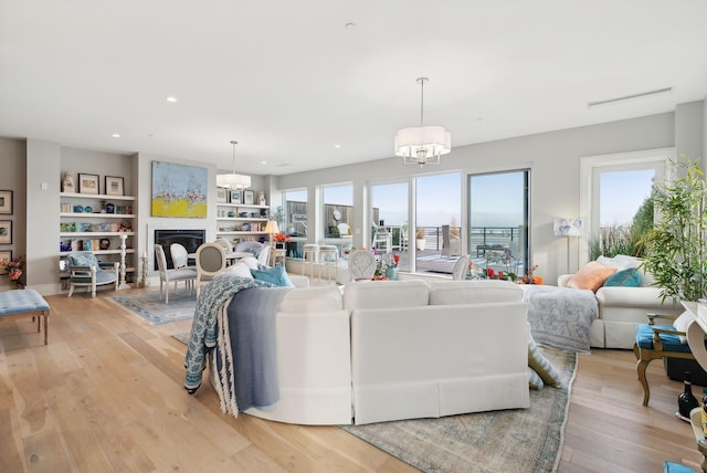 living room featuring a chandelier, built in shelves, and light hardwood / wood-style floors