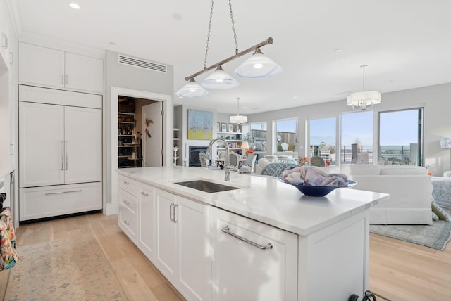 kitchen featuring paneled refrigerator, a kitchen island with sink, sink, white cabinetry, and hanging light fixtures