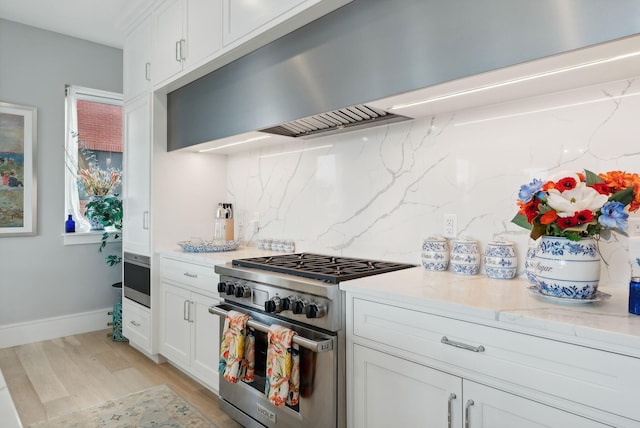 kitchen with light stone countertops, backsplash, high end stainless steel range oven, light hardwood / wood-style flooring, and white cabinets