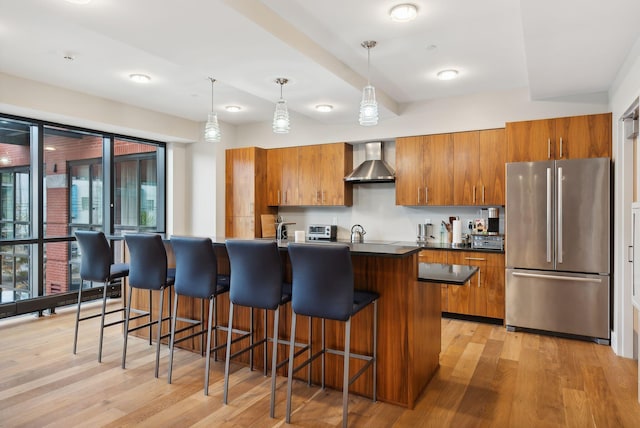 kitchen with stainless steel fridge, light hardwood / wood-style flooring, wall chimney exhaust hood, and hanging light fixtures