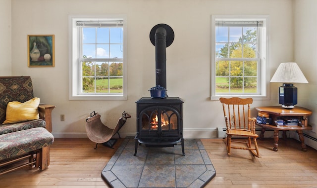 living area with light hardwood / wood-style flooring, a wood stove, and a baseboard heating unit