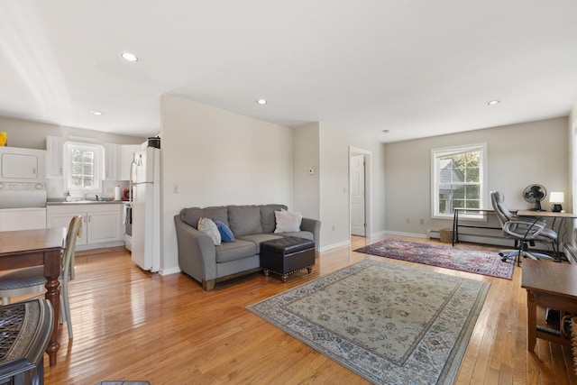 living room with light hardwood / wood-style flooring, sink, and stacked washing maching and dryer