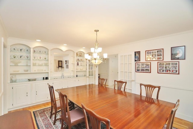 dining room with sink, crown molding, a notable chandelier, and light wood-type flooring