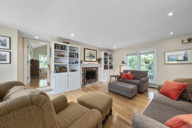 living room with light hardwood / wood-style flooring, a wealth of natural light, baseboard heating, and a fireplace