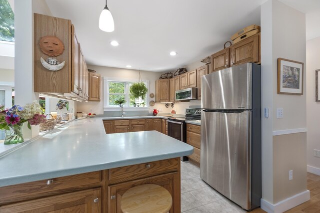 kitchen with pendant lighting, sink, kitchen peninsula, stainless steel appliances, and light hardwood / wood-style floors