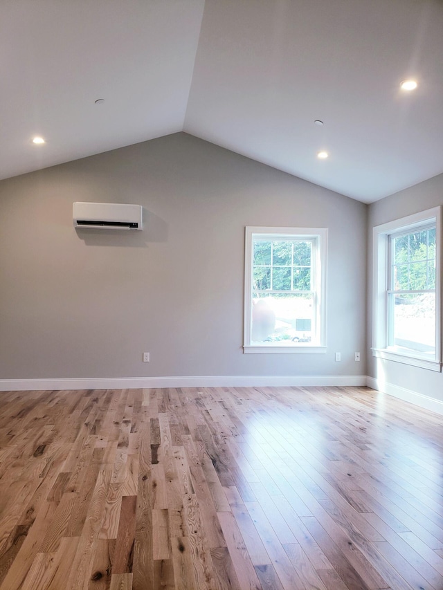 unfurnished room with vaulted ceiling, light hardwood / wood-style floors, and a wall mounted air conditioner