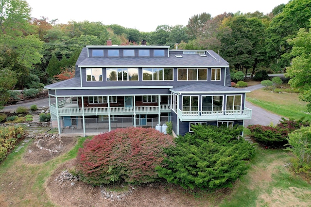 back of property with a sunroom, roof with shingles, a chimney, and a wooded view