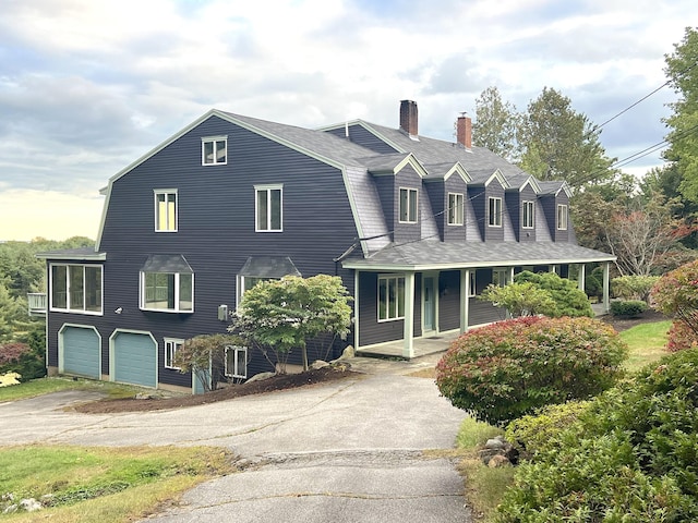 view of front of home featuring a chimney, aphalt driveway, a porch, a garage, and a gambrel roof