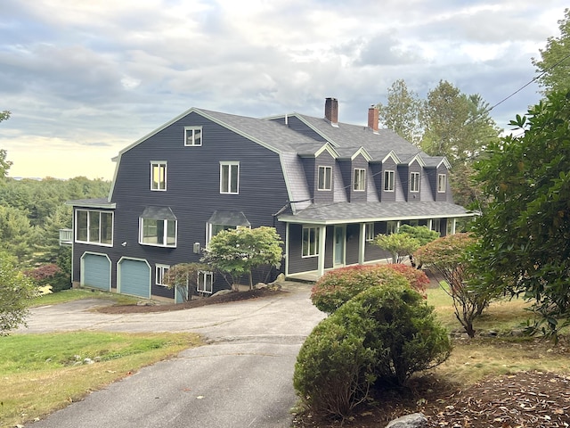 cape cod-style house featuring a gambrel roof, a garage, roof with shingles, a chimney, and driveway