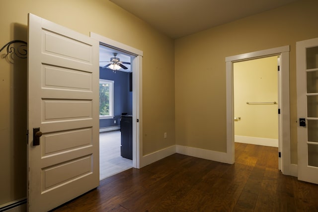 interior space with a ceiling fan, a baseboard heating unit, baseboards, and dark wood-style floors