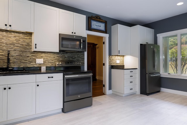 kitchen with light wood-type flooring, white cabinetry, dark countertops, a sink, and stainless steel appliances