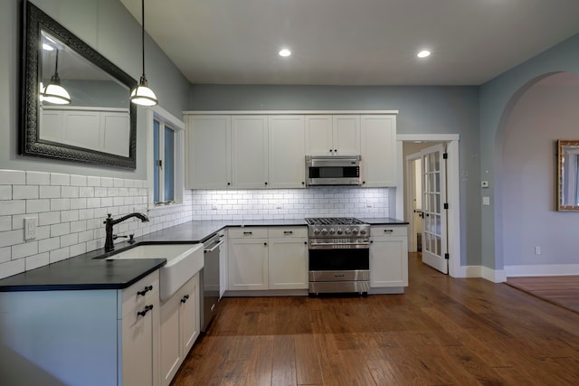 kitchen with appliances with stainless steel finishes, white cabinetry, dark hardwood / wood-style flooring, and pendant lighting