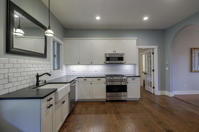 kitchen featuring arched walkways, white cabinets, appliances with stainless steel finishes, a sink, and dark countertops