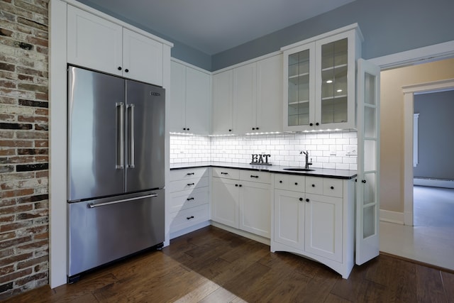 kitchen featuring glass insert cabinets, a sink, high quality fridge, dark countertops, and dark wood-style floors