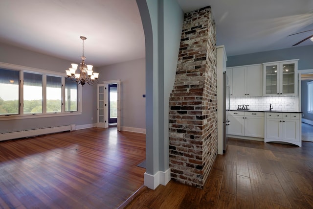 unfurnished dining area featuring ceiling fan with notable chandelier, baseboard heating, and dark wood-type flooring